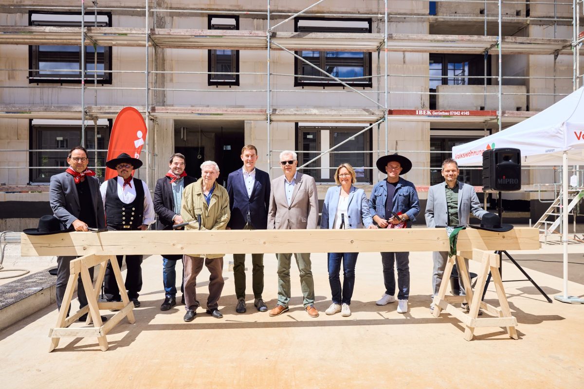 Richtfest Staudenplatz. Verschiedene Personen, darunter Geschäftsführer der Volkswohnung Stefan Stortz und Baubürgermeister Daniel Fluhrer stehen hinter einem horizontal aufgelegten Balken.