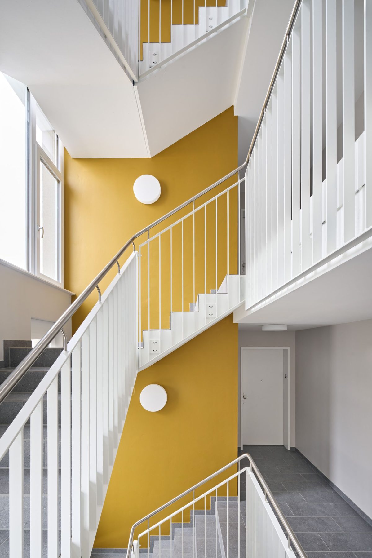 Treppenhausinnenansicht eines Mehrfamilienwohnhauses. Die Wände sind gelb und wei gestrichen. Die Treppe ist im Fokus und in der Mitte des Bildes.