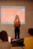 Eine junge Frau hält eine Power Point Präsentation vor einem Publikum.