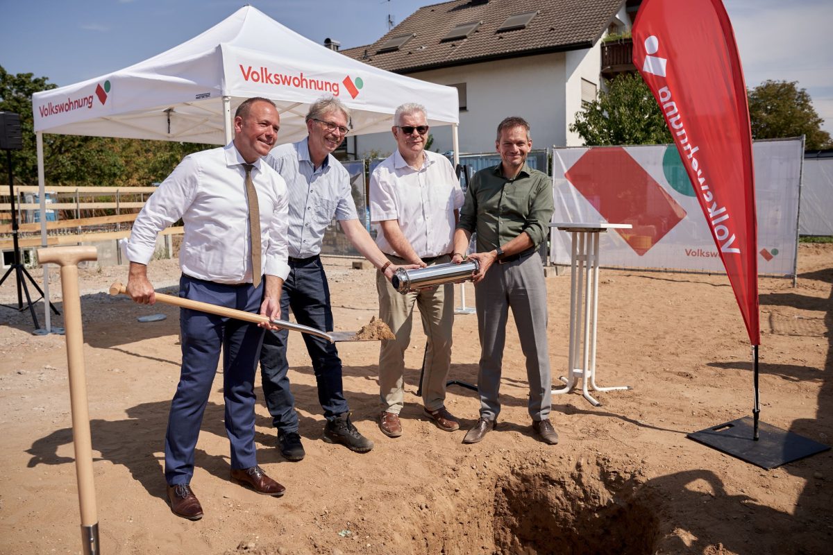Vier Personen stehen an einer Grube in der der Grundstein für die Wachhausstraße liegt. Eine Person schaufelt Erde darauf.