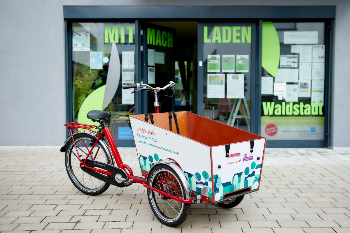Vor dem Mitmach-Laden in der Waldstadt steht das Quartiersrad Waldstadt, dass sich alle ausleihen können. Das Rad hat vorne einen sehr großen Lastenkorb.