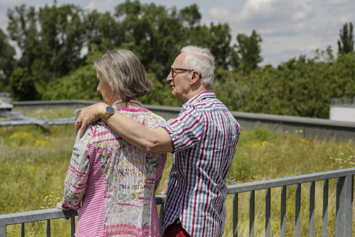Ein älteres Ehepaar steht auf einer Dachterrasse und schaut sich die blühende Dachbegrünung an.