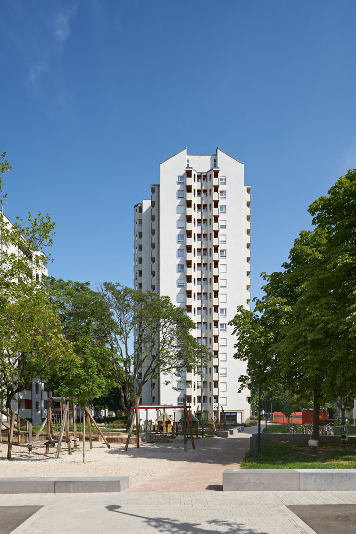 Ein Hochhaus im Rintheimer Feld, das nach der Modernisierung strahlend weiß ist. Im Vordergrund ist der neue, große Quartiersspielplatz.