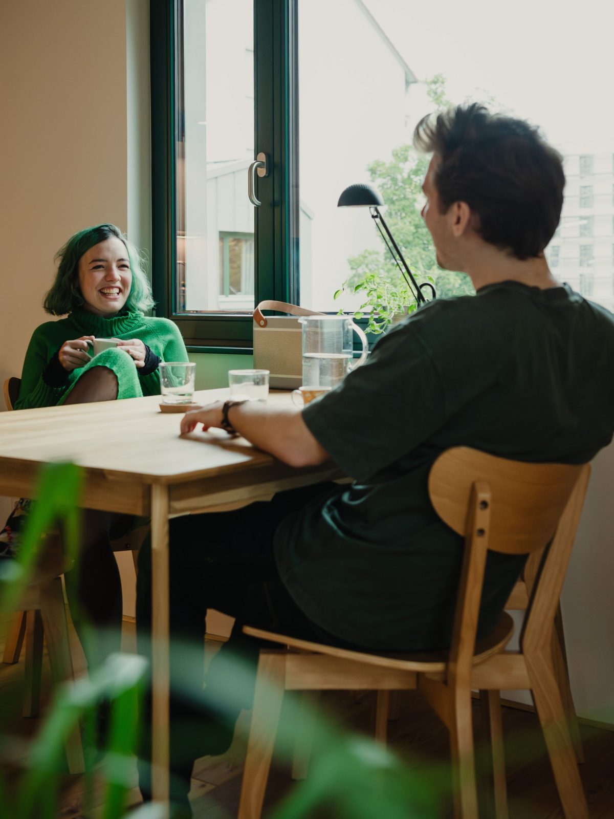 Ein Mann und eine Frau sitzen am Tisch gegnüber und unterhalten sich. Im Wohnzimmer des Neubauprojektes Garagenaufstockungen in Karlsruhe Rintheim.