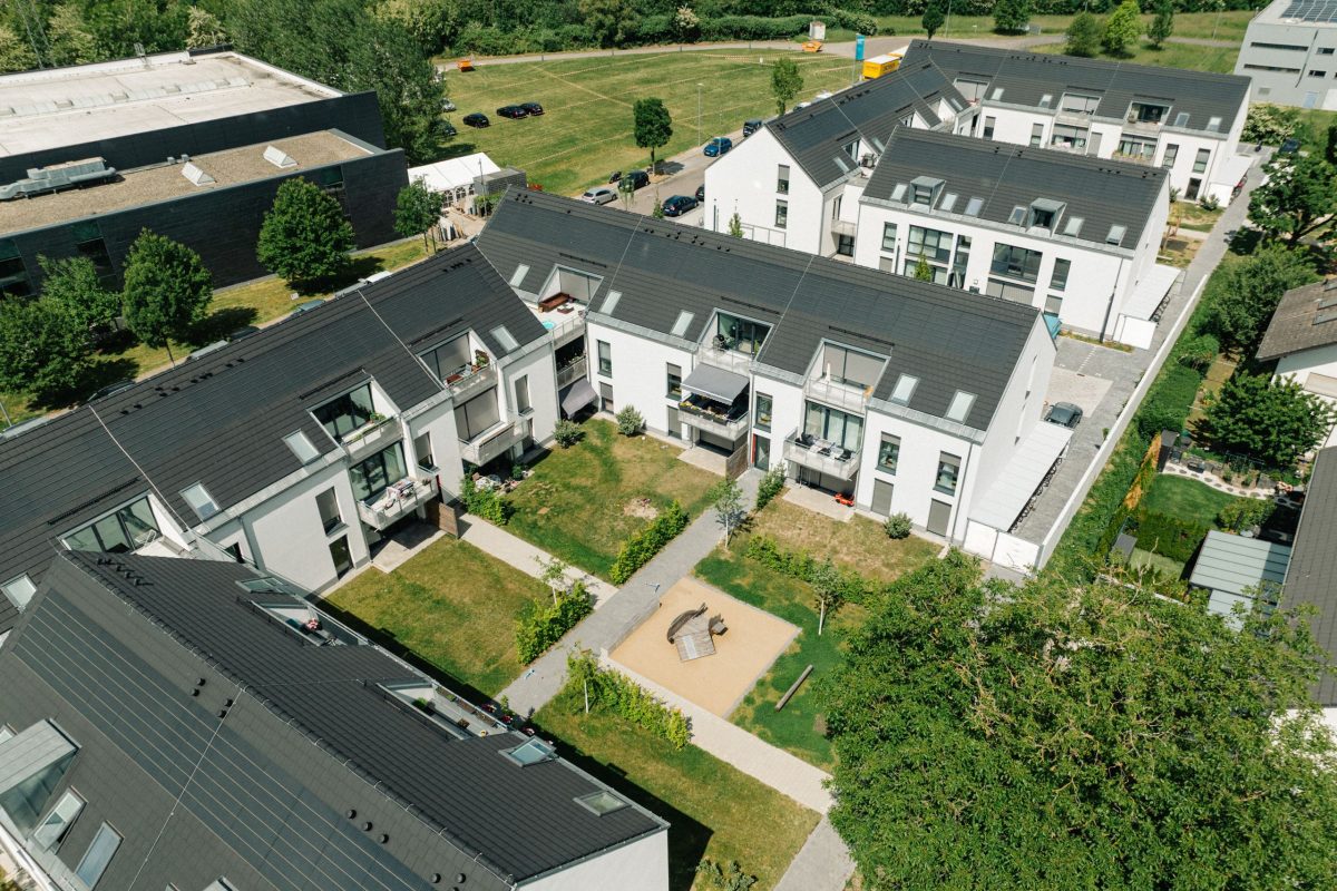 Drohnenansicht der Wachhausstraße von oben. Man sieht die u-fürmigen Gebäude, Rasenflächen und einen Spielplatz.