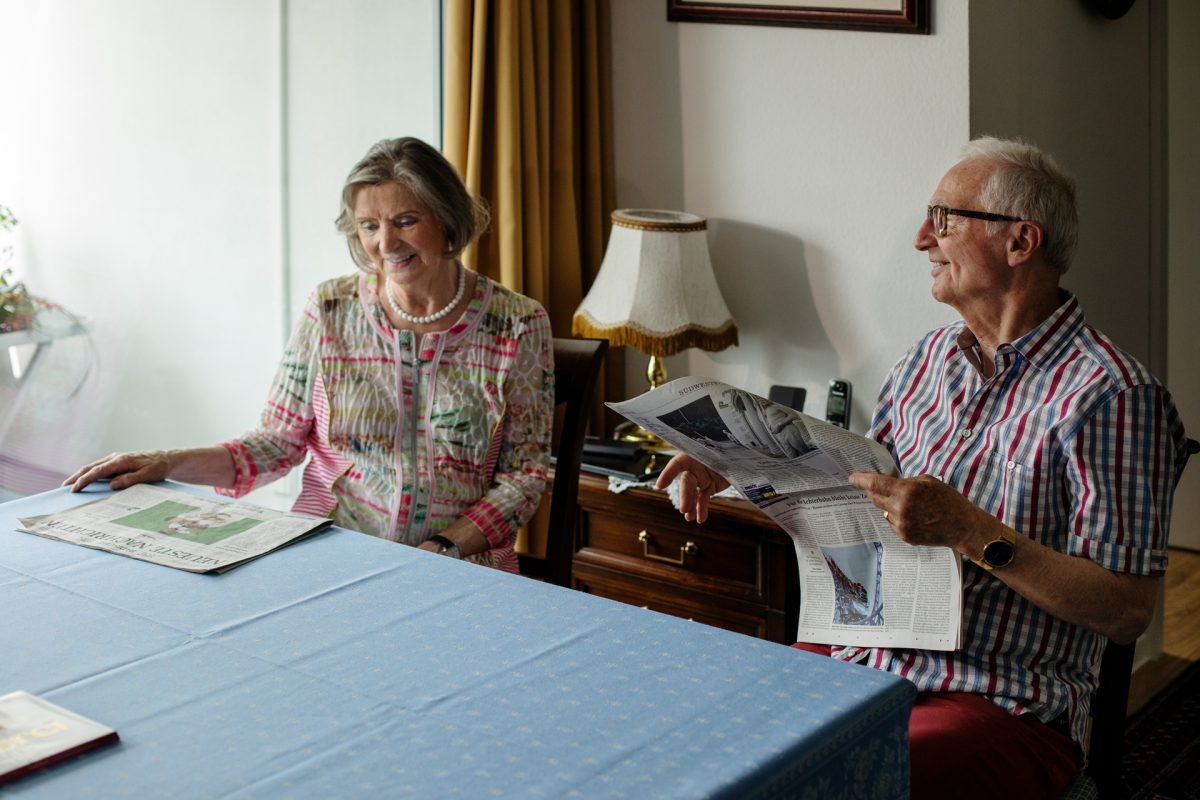 Ein älteres Ehepaar sitzt am Esstisch und liest Zeitung.