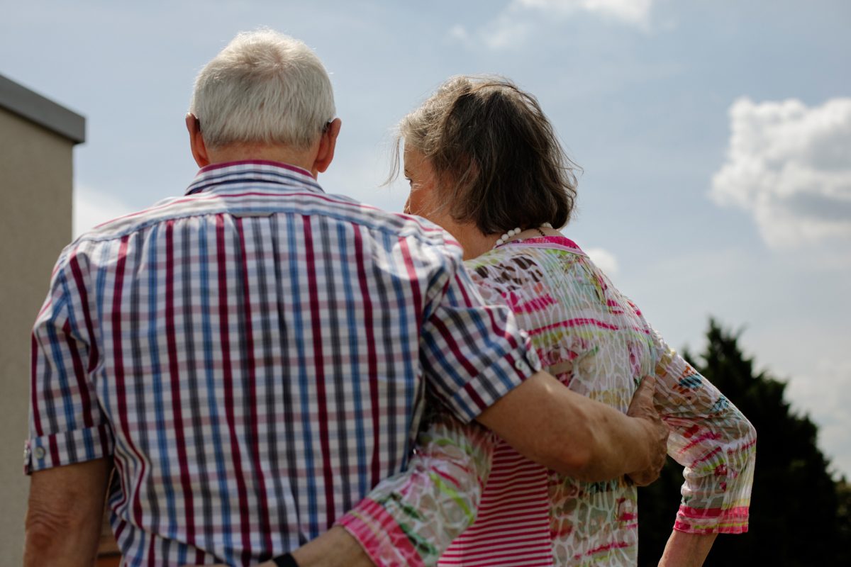 Ein älteres Ehepaar umarmt sich und ist von hinten zu sehen.