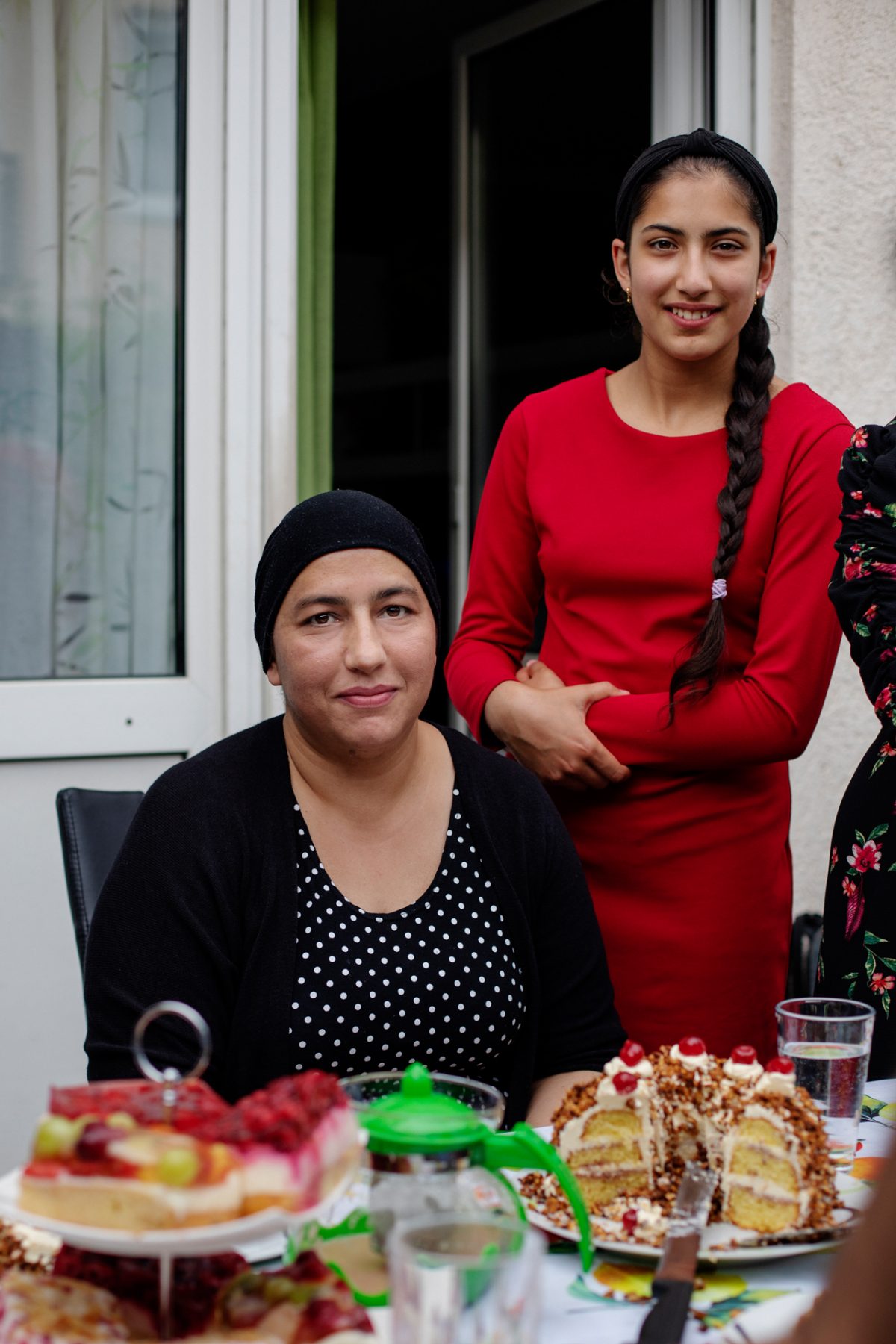 Eine Mutter sitzt am Kaffeetisch, ihre Tochter steht lächelnd hinter ihr.