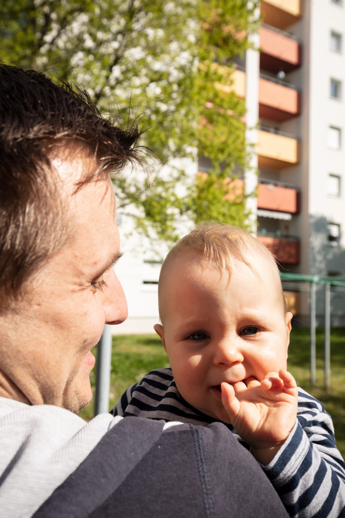 Ein junger Vater hält sein Kleinkind auf dem Arm, das an den Fingern lutscht.