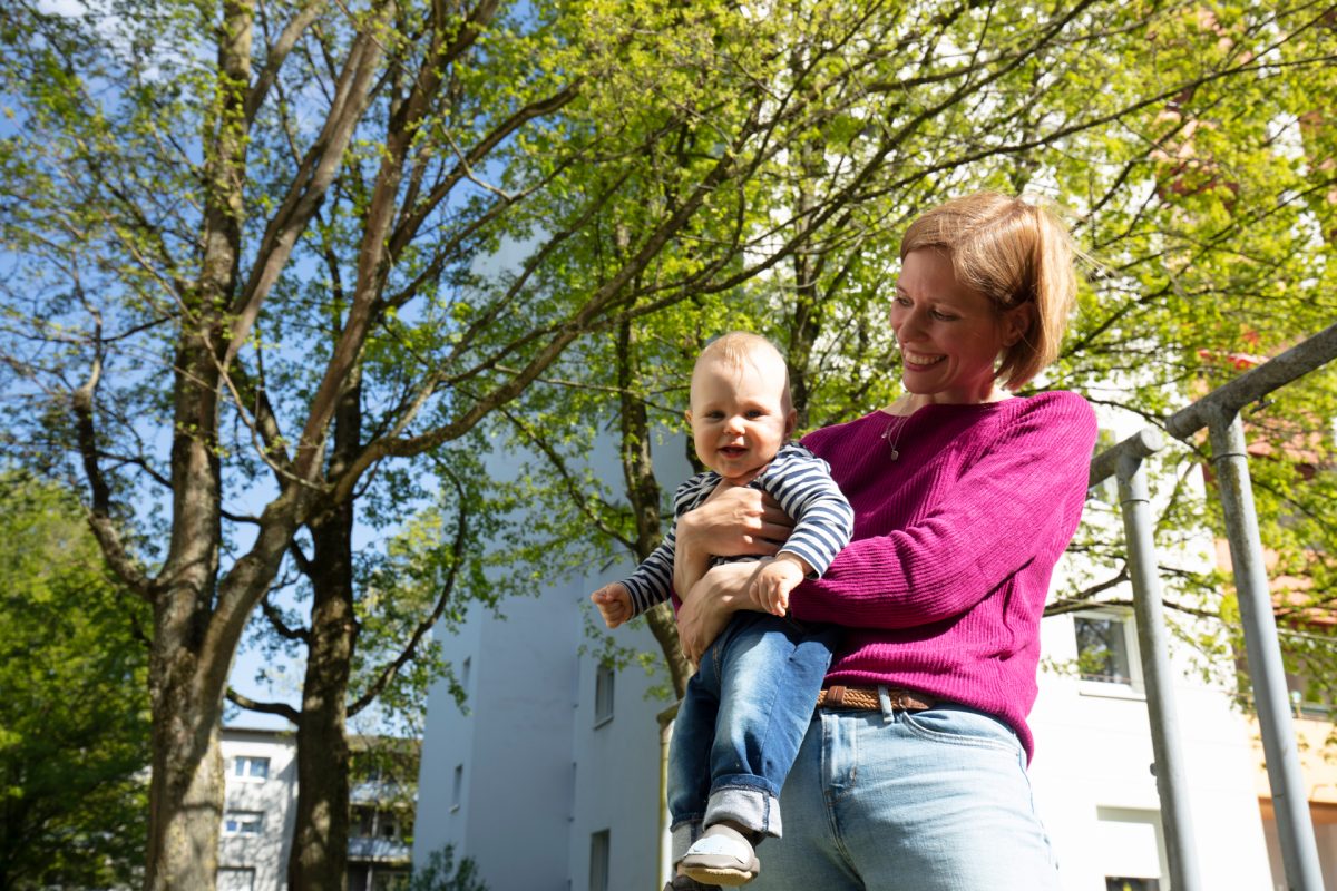 Eine junge Frau hält ihr Kleinkind auf dem Arm und lächelt.