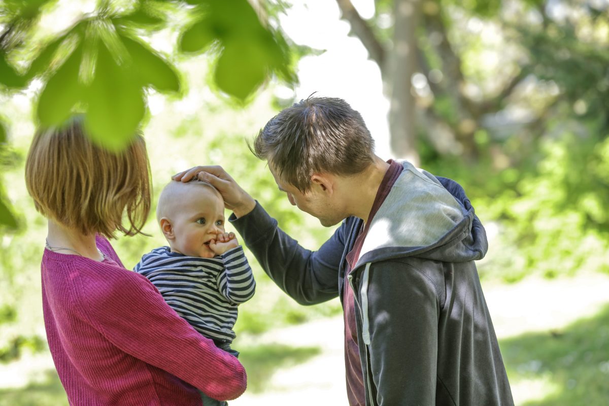 Eine junge Mutter hält ihr Kleinkind auf dem Arm, der Vater streichelt ihm über den Kopf.