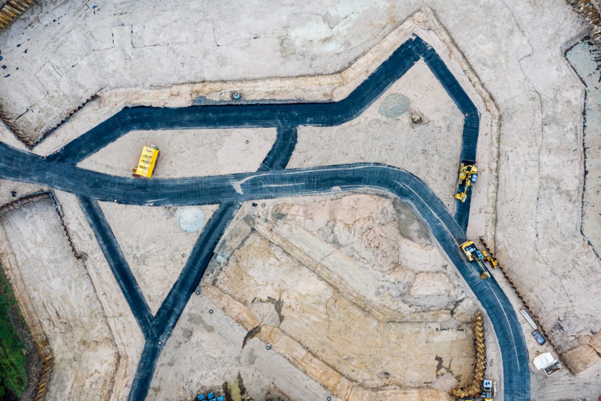 Luftbild einer Baustelle, auf der man die Baustraßen dunkel sieht, umrandet von hellbrauner Erde.