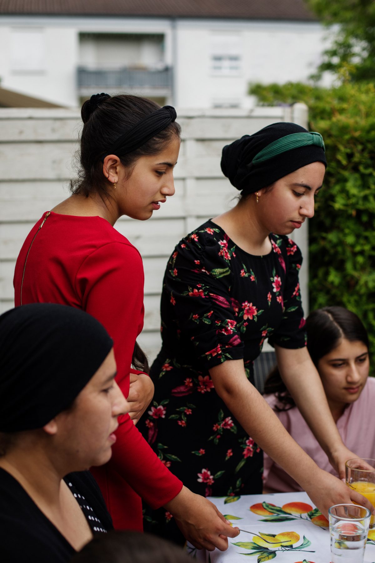 Zwei junge Frauen stehen am Tisch im Garten ihres Mietshauses, gemeinsam mit der Familie.