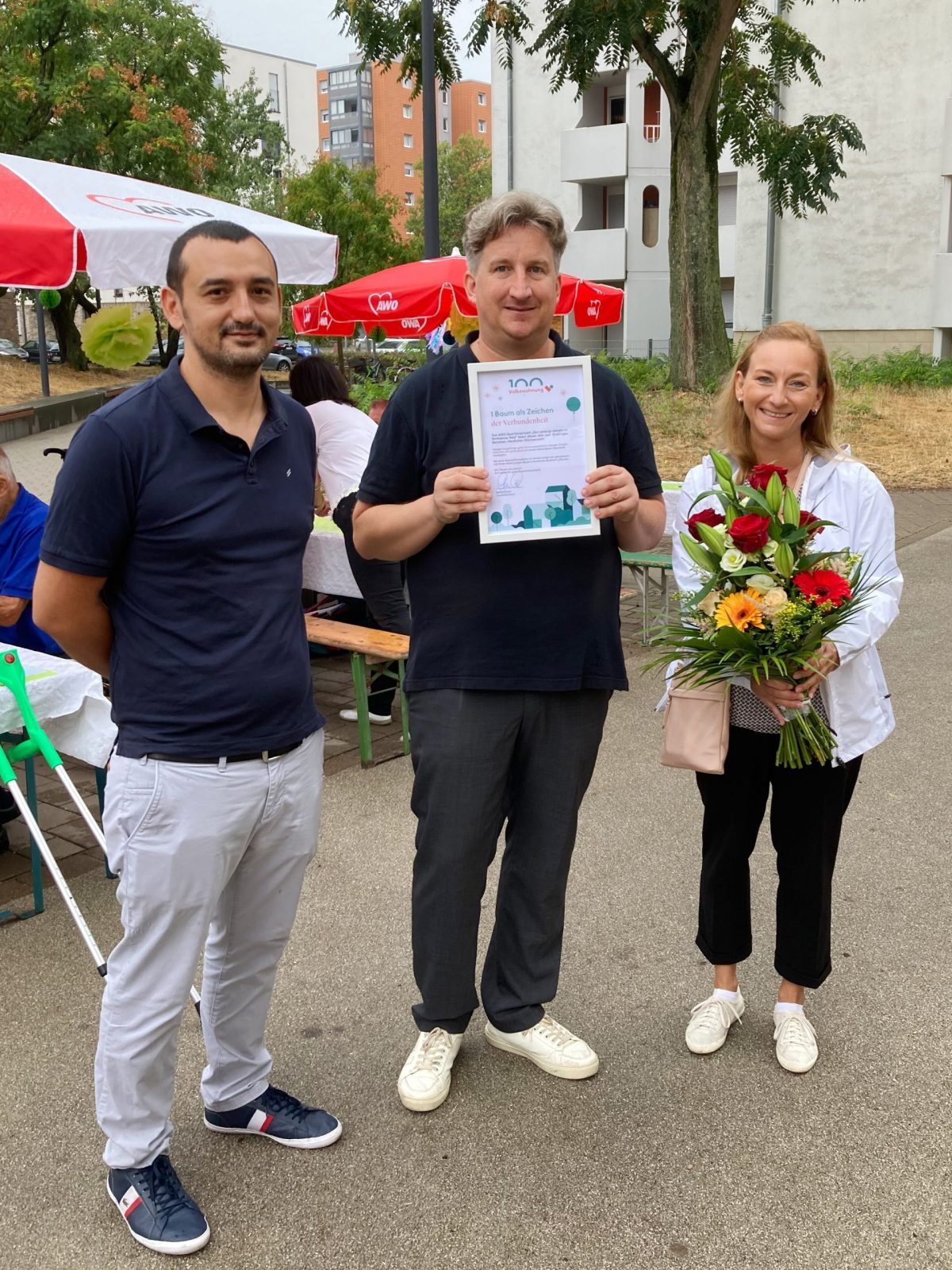 Der Quartiersmanager erhält eine Urkunde von zwei Volkswohnungs-Mitarbeitern.