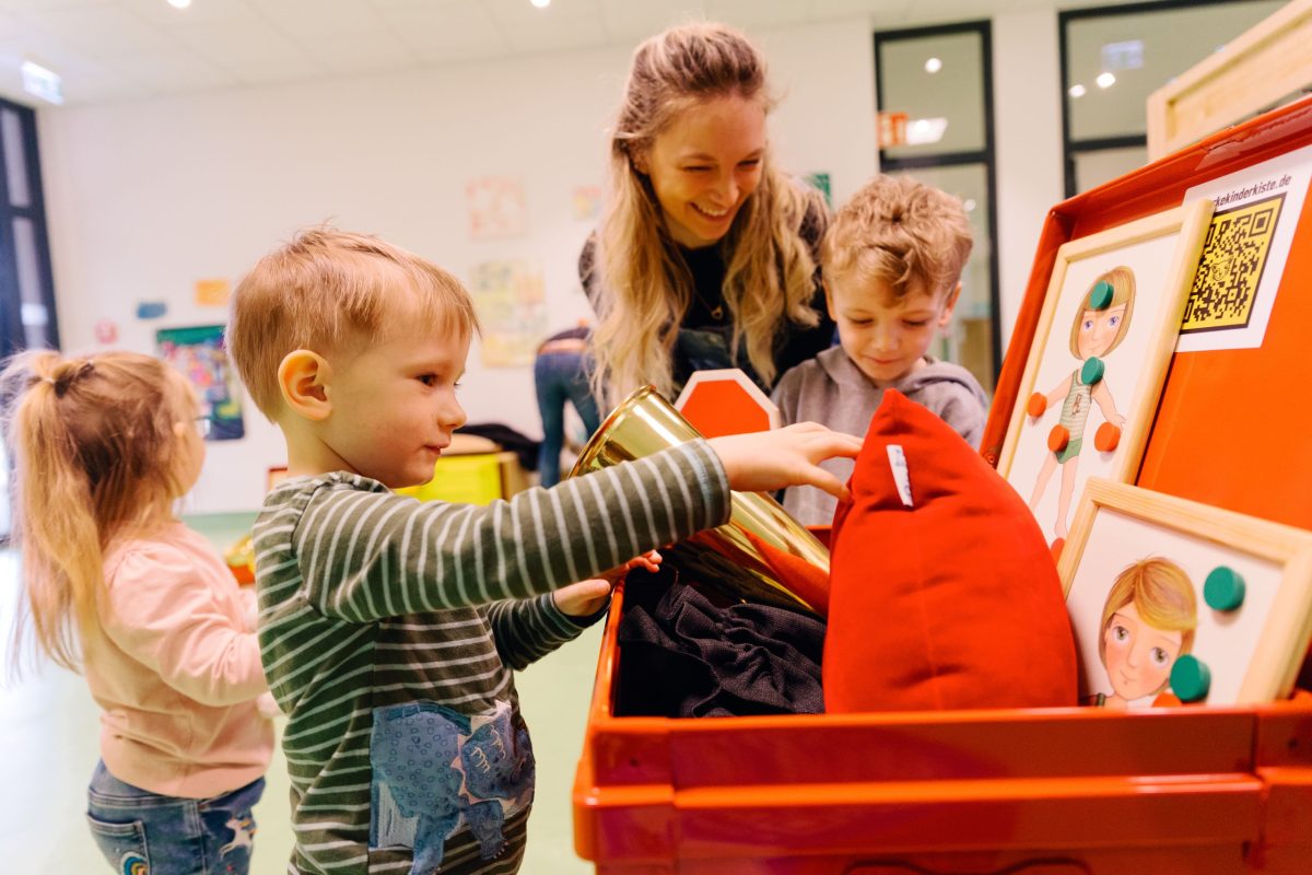 Mehrere Kinder schauen mit einer Erzieherin den Inhalt der Kiste an.
