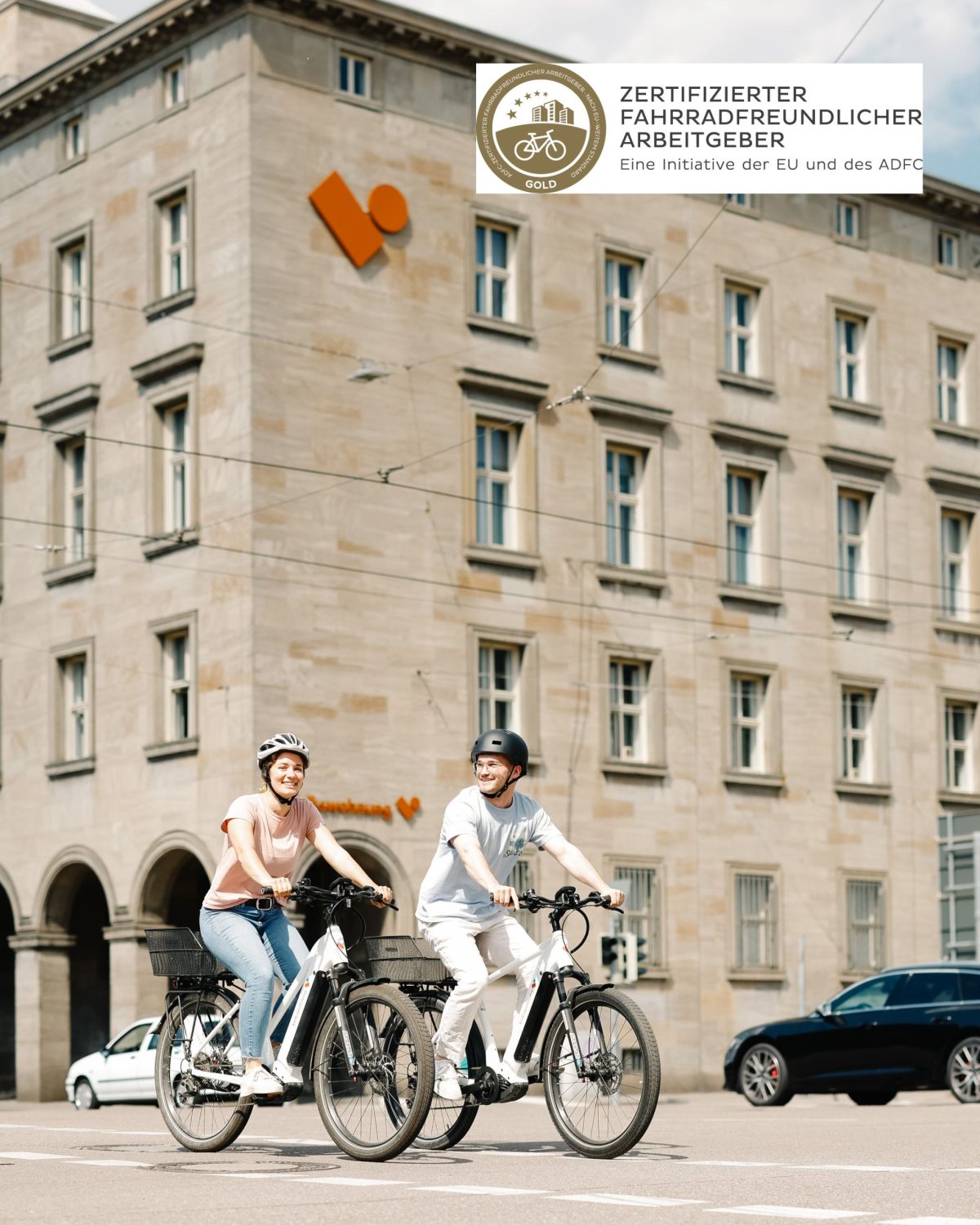 Zwei Mitarbeiter der Volkswohnung fahren mit dem Fahrrad an der Zentrale vorbei. Im Bild das Logo 