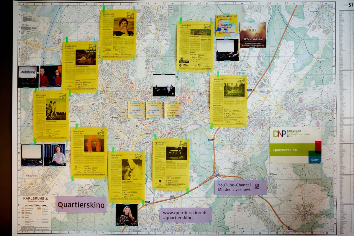 Auf einem großen Karlsruher Stadtplan sind mehrere gelbe Din A4-Zettel angebracht, die über Filmangebote in den Quartieren informieren.
