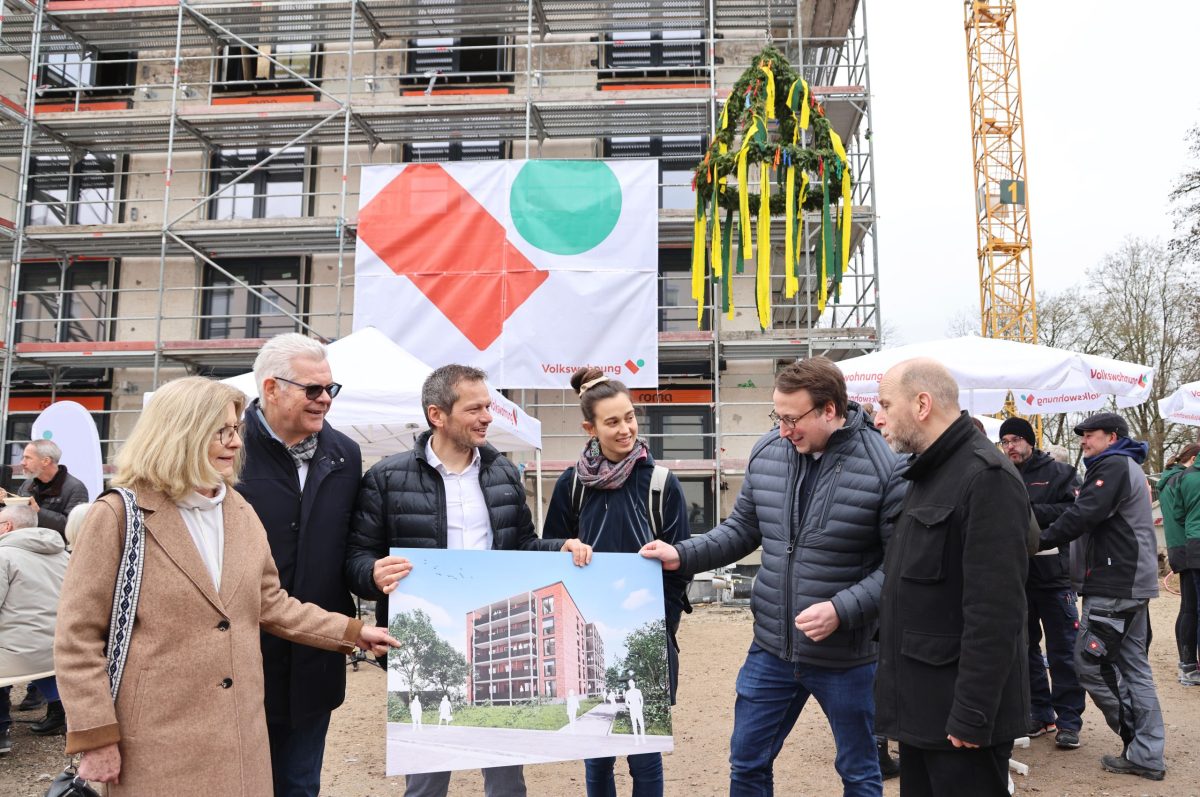 Beim Richtfest hält Stefan Storz eine großformatige Visualisierung in der Hand und zeigt sie mehreren Gemeinderäten.