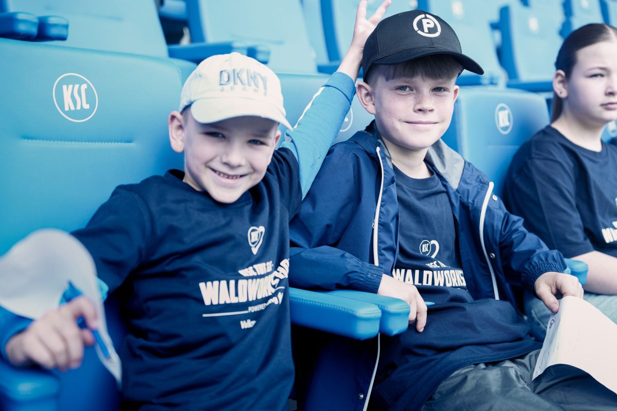 Drei Kinder sitzen im BBBank Wildpark und freuen sich auf den Spielbeginn.