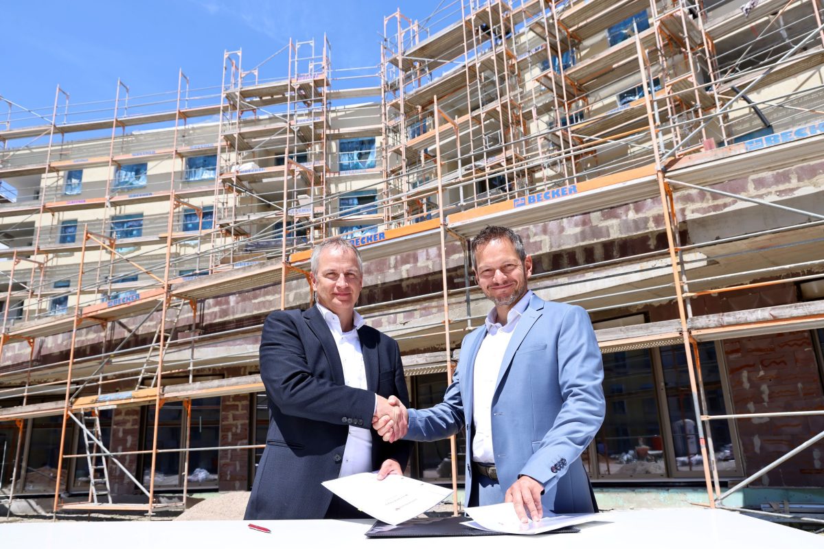 Der Geschäftsführer der Volkswohnung und der Direktor der Evangelischen Kirchenverwaltung Karlsruhe stehen auf einer Baustelle und reichen sich die Hand.