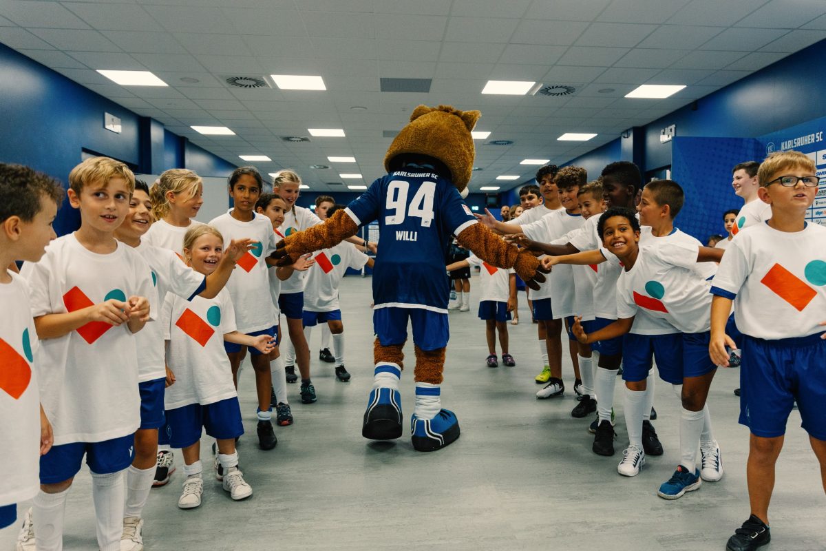 Rund 30 Kinder stehen im Spielertunnel zum BBBank Wildpark und werden vom Maskottchen Willi Wildpark per Handschlag begrüßt.