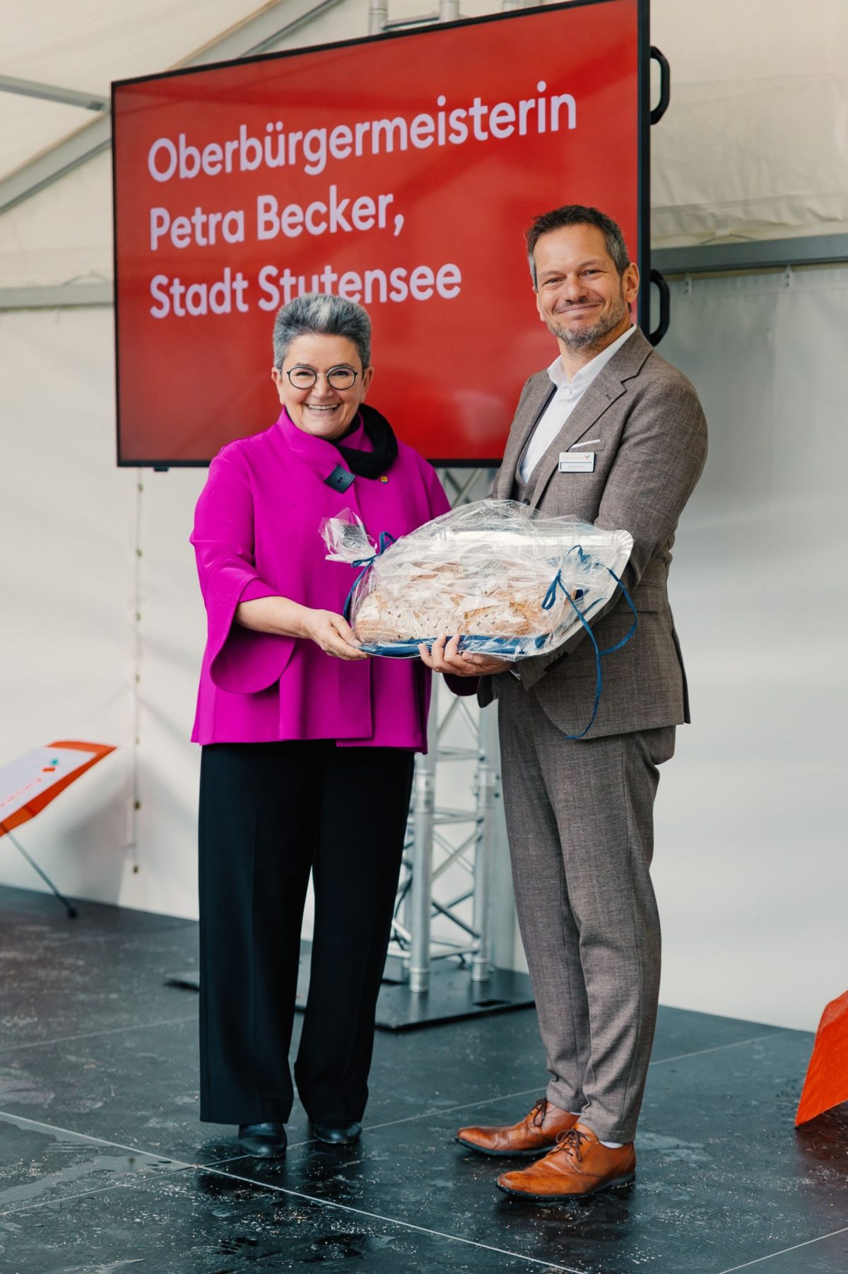 Die Oberbürgermeisterin von Stutensee, Petra Becker, übergibt das symbolische Brot und Salz zum Einzug und zur Fertigstellung des Bauprojektes an den Geschäftsführer der Volkswohnung, Stefan Storz,