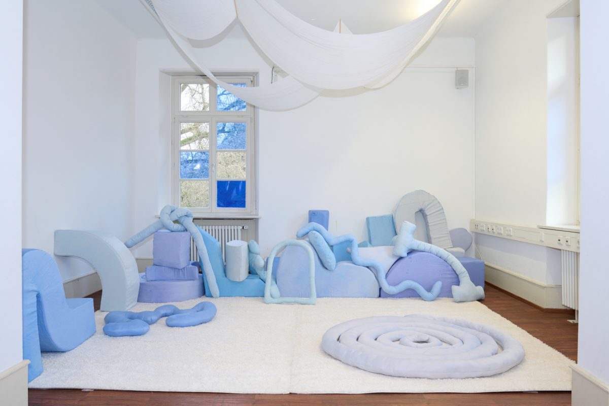 Ein schöner Raum mit weißem Teppich und vielen verschiedenen blauen Kissen. Er gehört zur Ausstellung