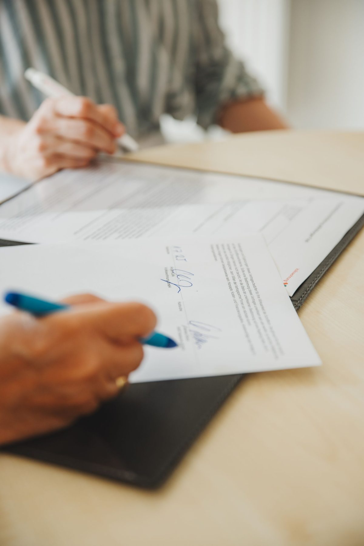 Zu sehen ist eine Detailaufnahme einer Vertragsunterzeichnung (Hände, Stift, Vertrag).