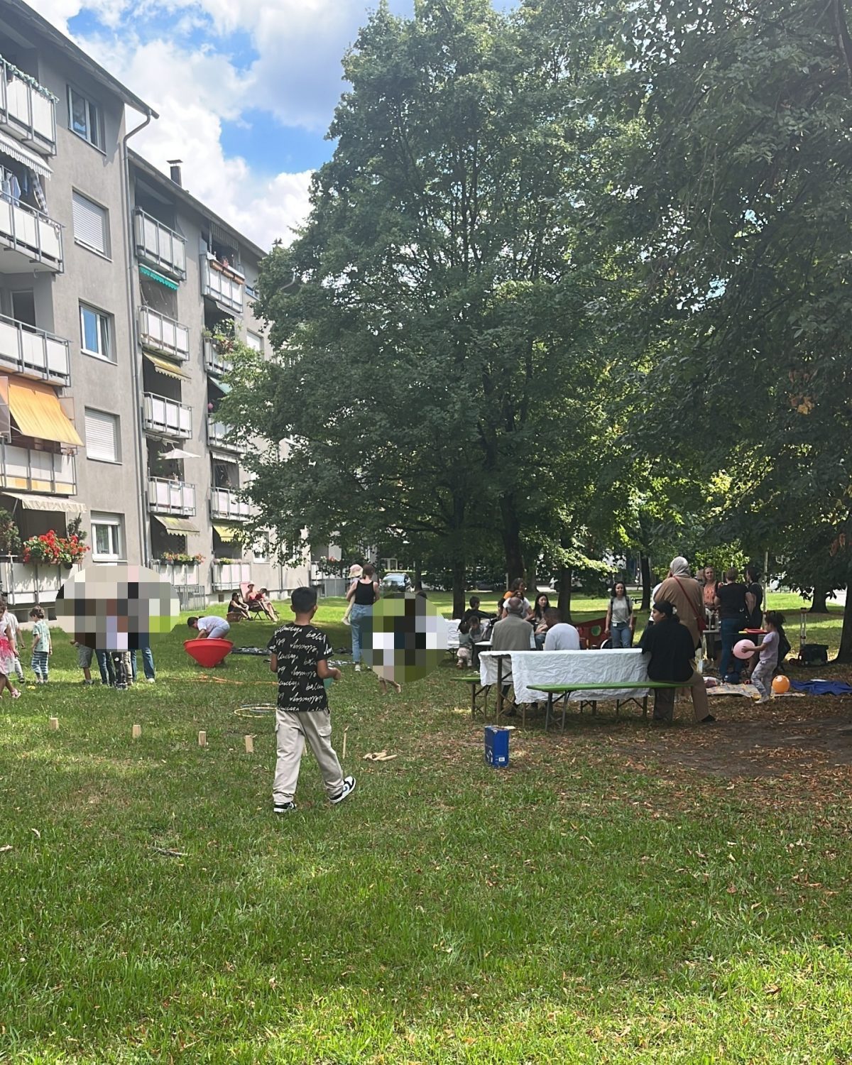Auf einer grünen Wiese wurde ein Picknick aufgebaut. Die Gäste sitzen an Biertischen.