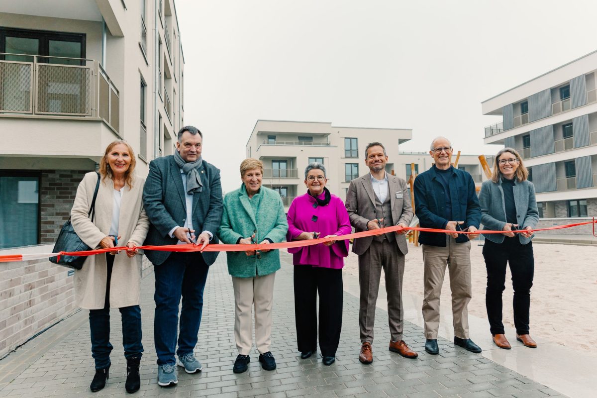 Sieben Personen stehen und halten gemeinsam ein rotes Band zur Eröffnung