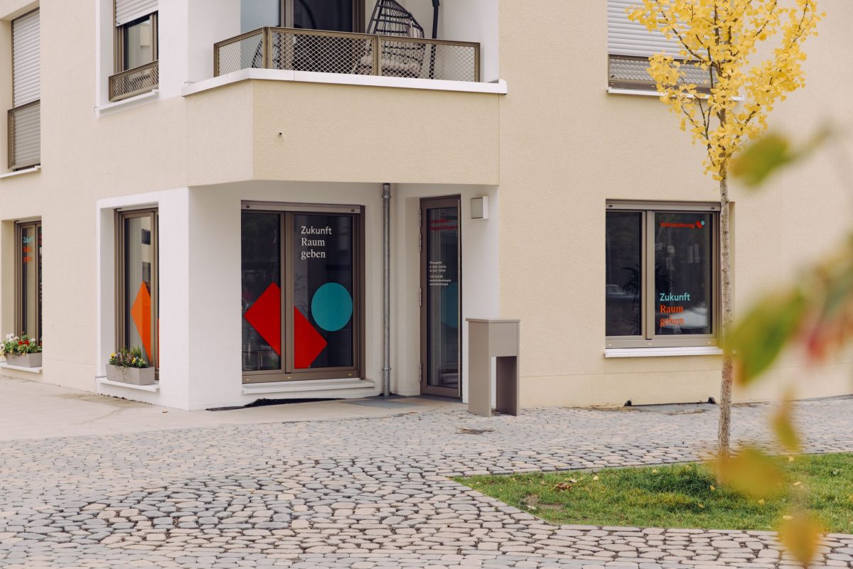 Außenansicht des Volkswohnungs-Servicebüros Daxlanden. Die Fenster sind großflächig mit dem Logo der Volkswohnung und dem Schriftzug Zukunft Raum geben beklebt.