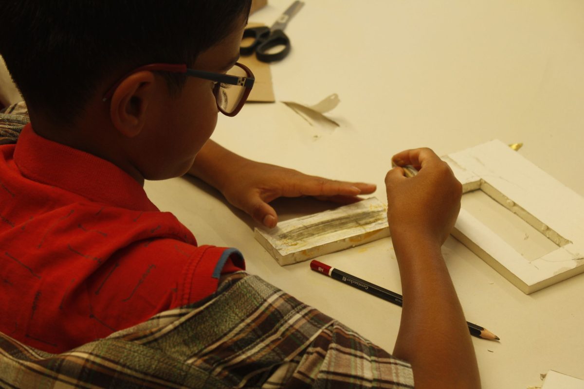 Ein Junge bemalt ein Stück Holz.