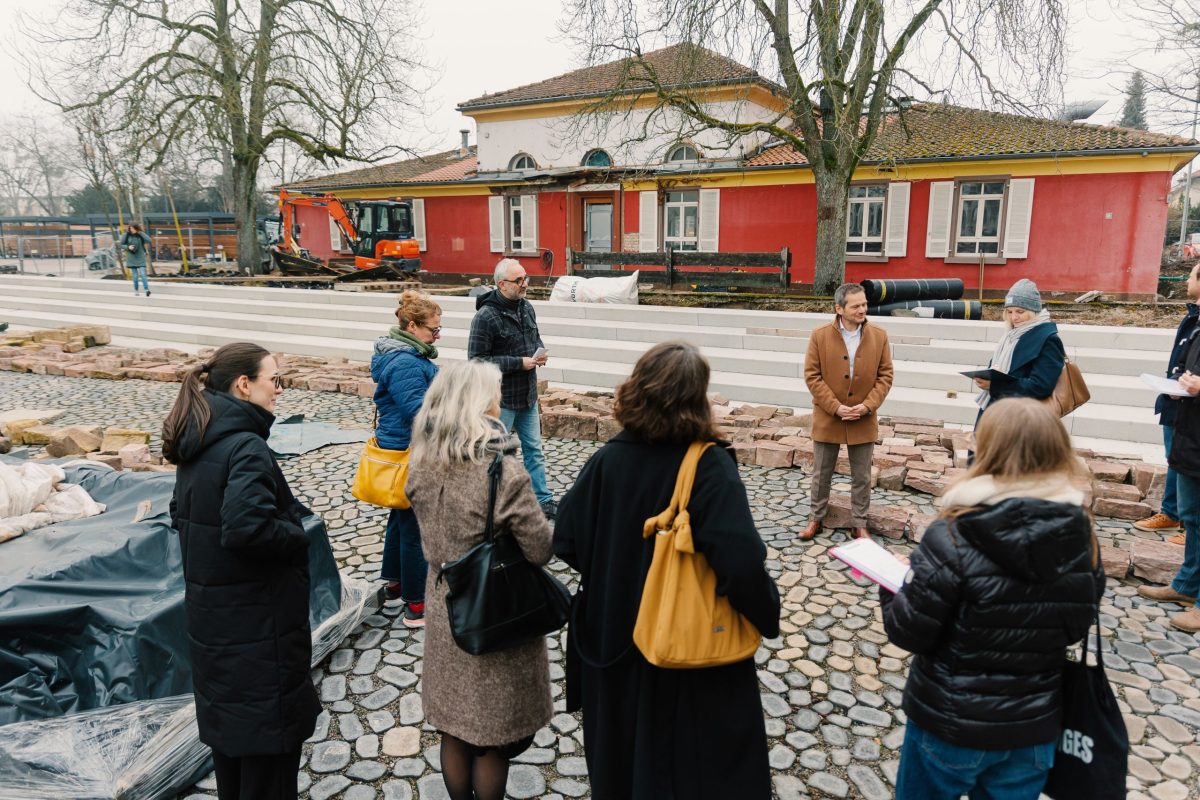 Mehrere Personen von der Presse stehen vor einem roten Gebäude.