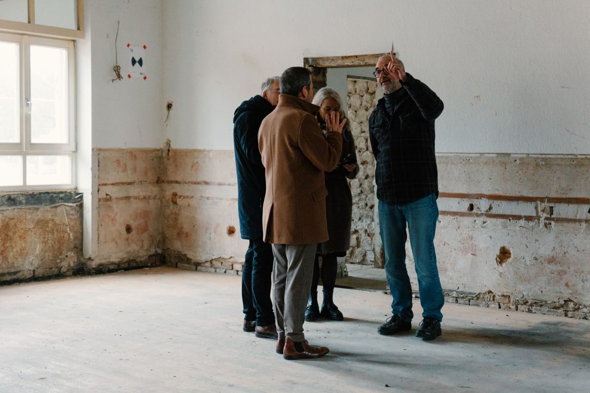 Vier Personen stehen in einem Raum, der gerade renoviert wird und unterhalten sich