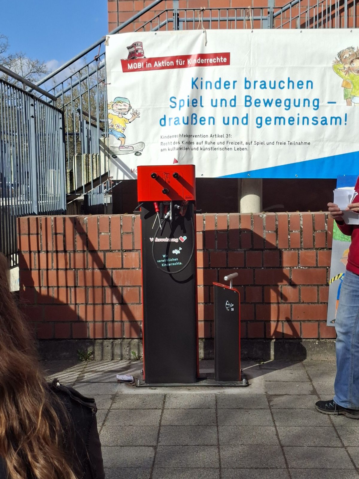 Neue Fahrradreparatursäule des Stadtjugendausschusses in Oberreut. Die Säule steht vor einer Backsteinmauer, im Hintergrund hängt ein Banner der auf die Einweihung hinweißt.