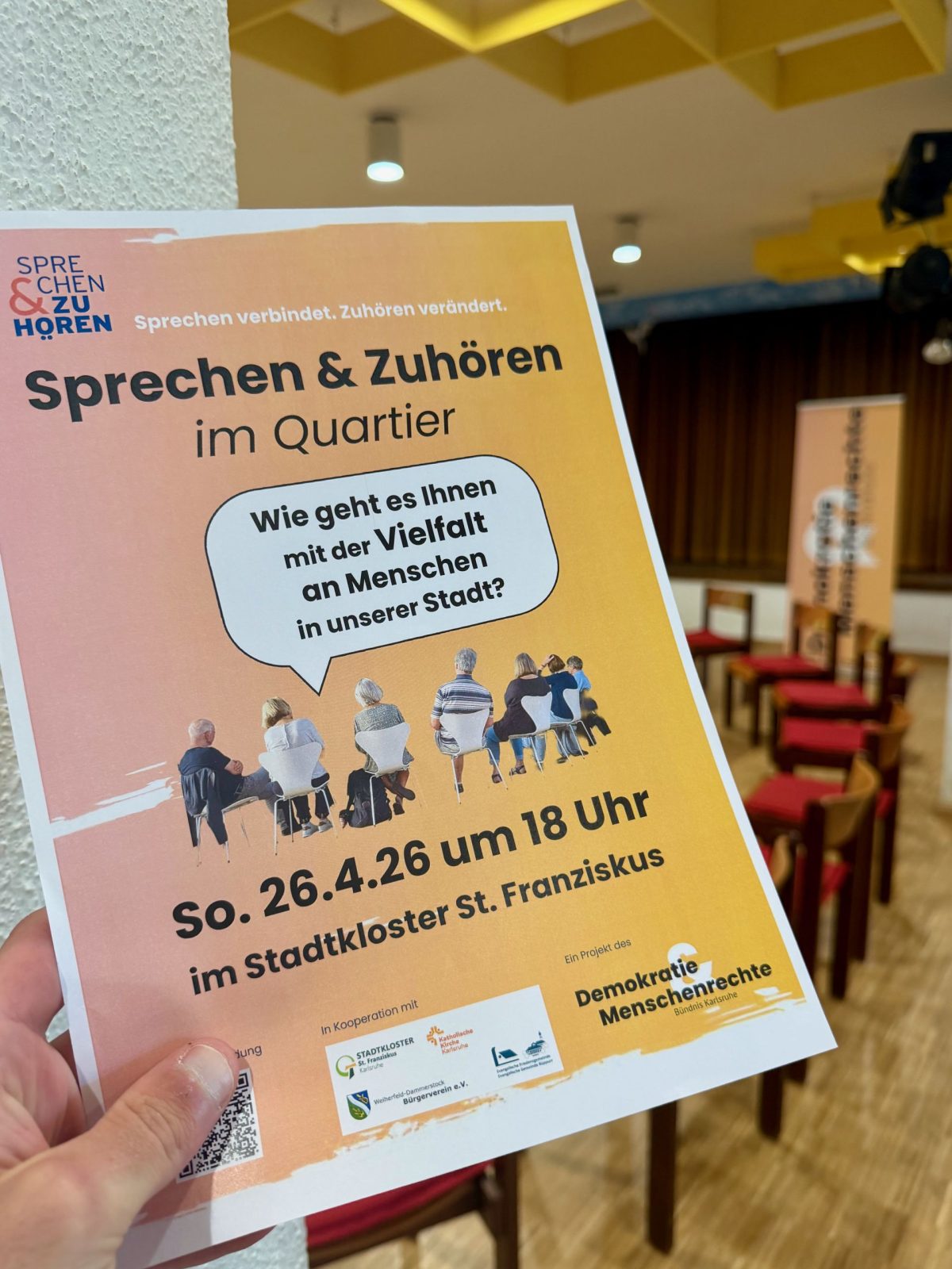 Flyer des Projekts Sprechen und zuhören im Quartier, der von einer Hand in den Vordergrund gehalten wird