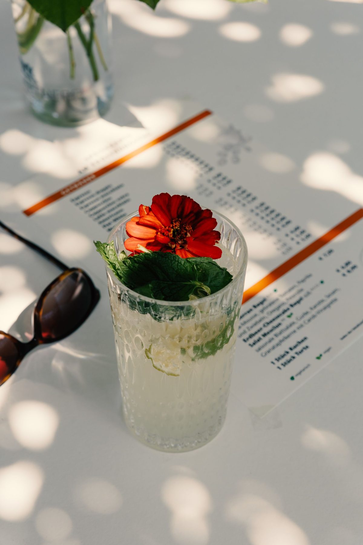 Auf einem Tisch liegt ein Menü den Cafés Samocca-Augustine, eine Sonnenbrille und eine Limonade in einem Glas.