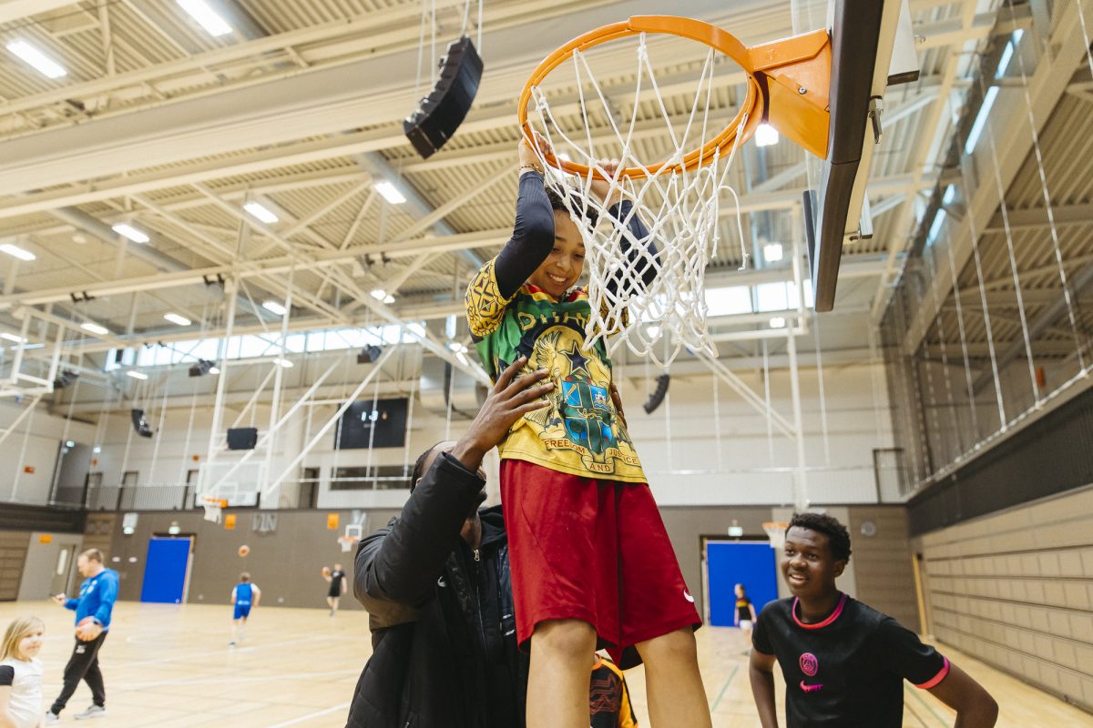 Ein Basketballprofi hebt ein Kind zum Basketballkorb, um einen Treffer zu machen.